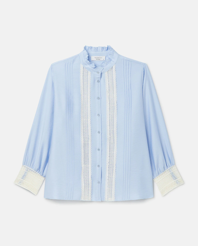 Blusa romántica de manga francesa con volante en el cuello. Se encuentra disponible en los colores azul y negro. Es de la marca Woman de El Corte Inglés. Precio: 59,99 €. 