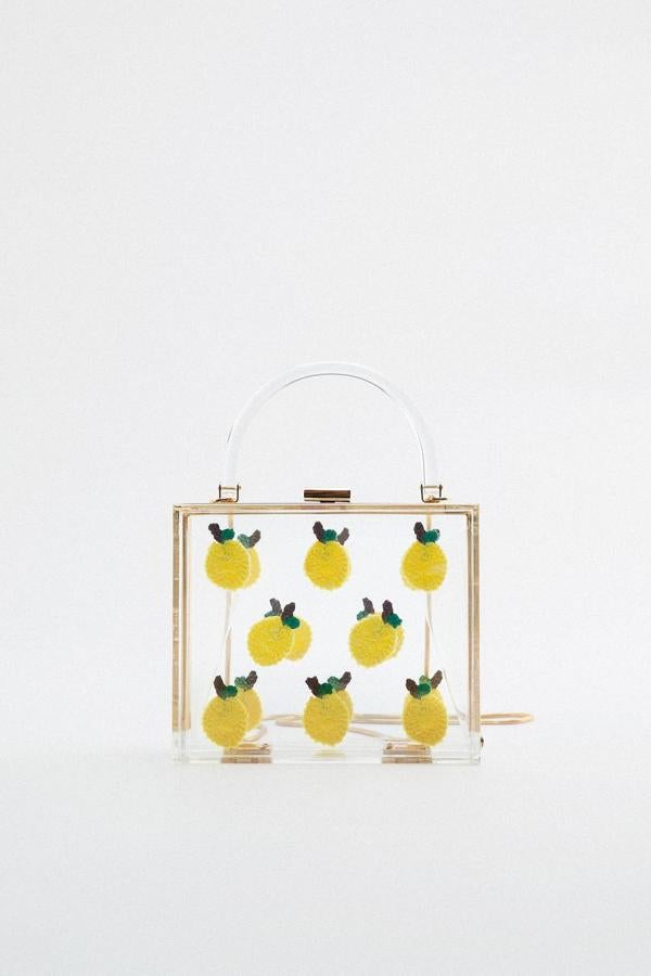 Bolso tipo caja de metacrilato transparente con asa de mano y cadena dorada a modo de bandolera, decorado con estampado de limones, de Zara. Su precio es de 35,95 euros.