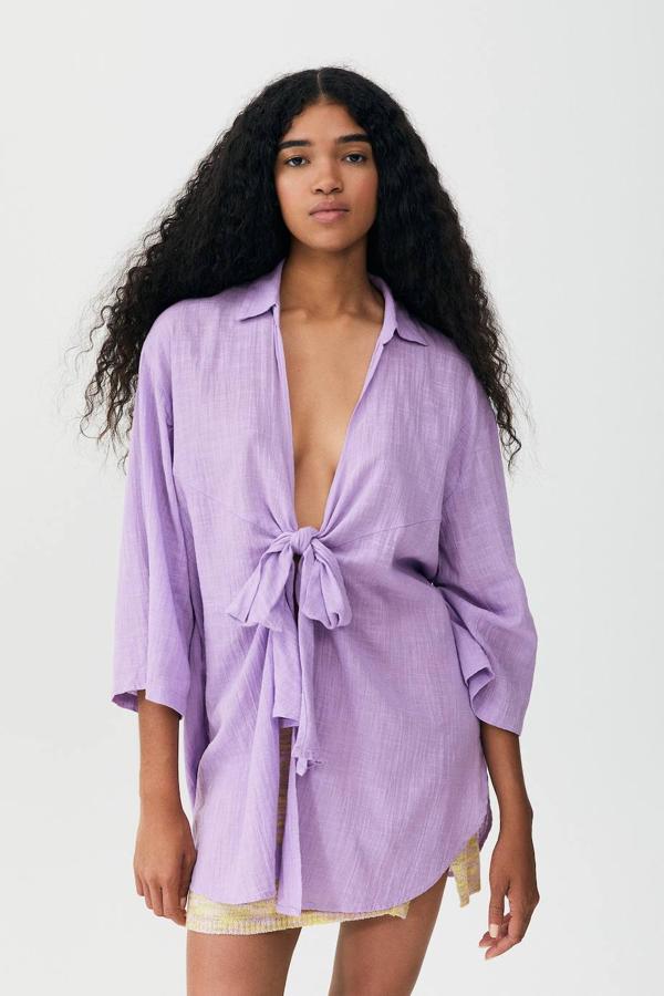 Blusa oversize en tejido ligero texturizado con cuello solapa, silueta relajada, manga francesa amplia y cierre mediante lazada frontal, de Pull&Bear. Está disponible en lila, rosa, blanco y marrón, a 25,99 euros.