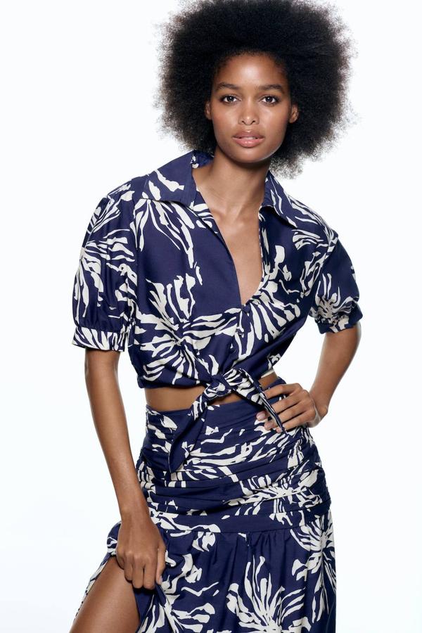 Camisa cropped con manga corta abullonada, cuello solapa, escote de pico, cierre de botones y bajo para anudar, decorada con estampado tropical en azul y blanco, de Zara. Cómprala a 29,95 euros.
