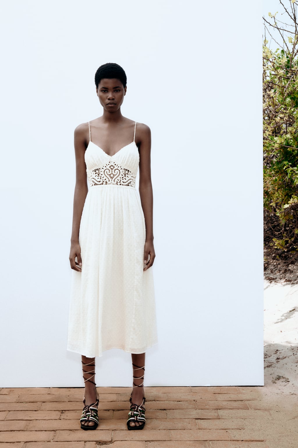 La versión más sofisticada del vestido de tirantes se tiñe de blanco y llega con detalles de encaje. Vestido midi en color blanco roto de Zara (45,99 euros)