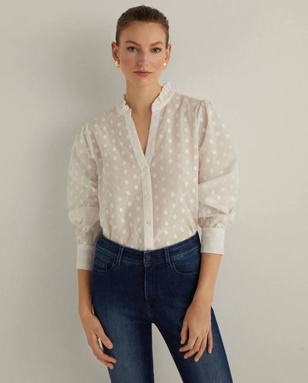 Blusa en tejido ligero semitransparente decorada con bordados de lunares a tono, color crudo. Tiene cuello subido con volante, escote de pico, manga larga terminada en puño y cierre frontal de botones. Puedes comprarla en El Corte Inglés, rebajada a 25,99 euros.