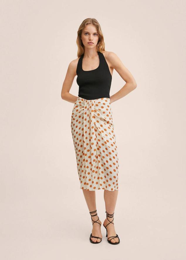 Falda midi en tejido ligero plisado con estampado de lunares color crudo y naranja. Tiene talle alto, silueta acomodada a la figura y detalle drapeado frontal, de Mango. Antes costaba 29,99 euros y ahora la puedes comprar a 19,99 euros.