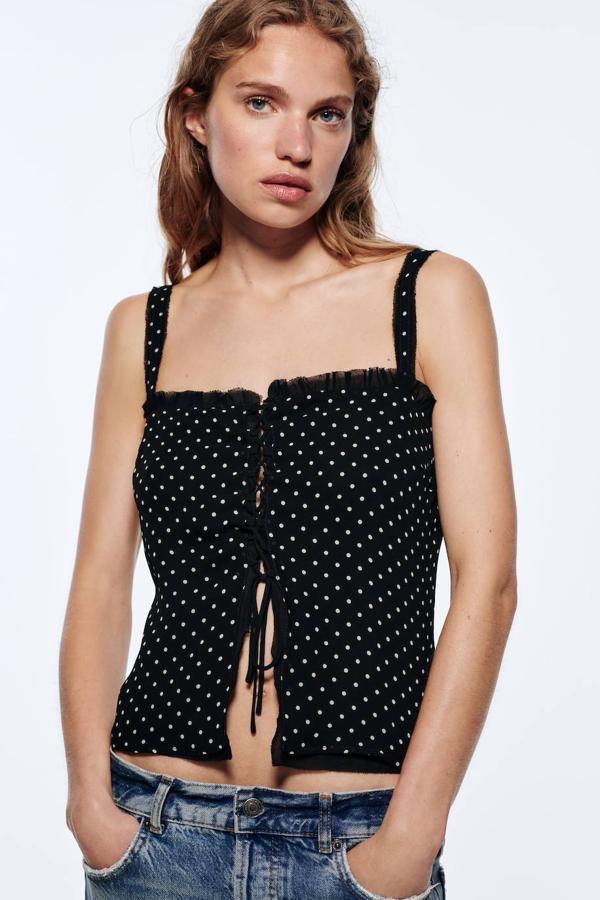 Top de lunares en negro y blanco con tirantes finos, escote recto, detalles de tul y cierre mediante lazada fontal, de Zara. Tiene un precio rebajado de 19,99 euros.