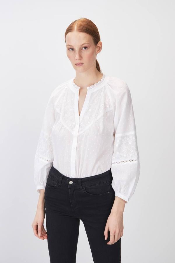 Blusa romántica en tejido 100% algodón blanco con cuello redondo decorado con puntilla, bordados, manga larga ligeramente abombada y cierre de botones. Puedes comprarla con descuento por 15,99 euros.
