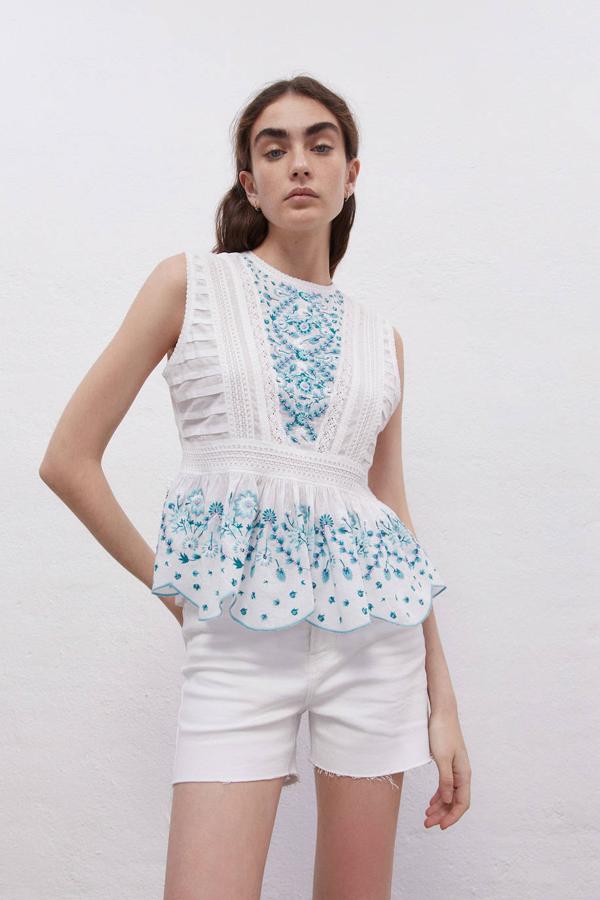 Blusa blanca con manga sisa, cuello redondo, bajo acabado en volante, detalles plisados y de puntillas, decorada con bordado de flores en azul. La encontrarás con descuento por 15,99 euros.