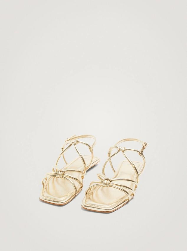 Sandalias planas con tiras de doble nudo en acabado metalizado dorado. Tienen un precio de 29,99 euros.