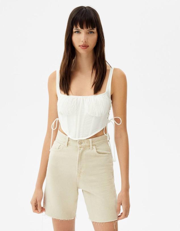 Top corsé con tirantes, escote cuadrado, copas marcadas con tejido fruncido, cuerpo con ballenas, lazadas en los laterales y detalle de elástico tipo nido de abeja en la espalda, color blanco, de Bershka. Cuesta con descuento a 7,99 euros. Cómpralo aquí