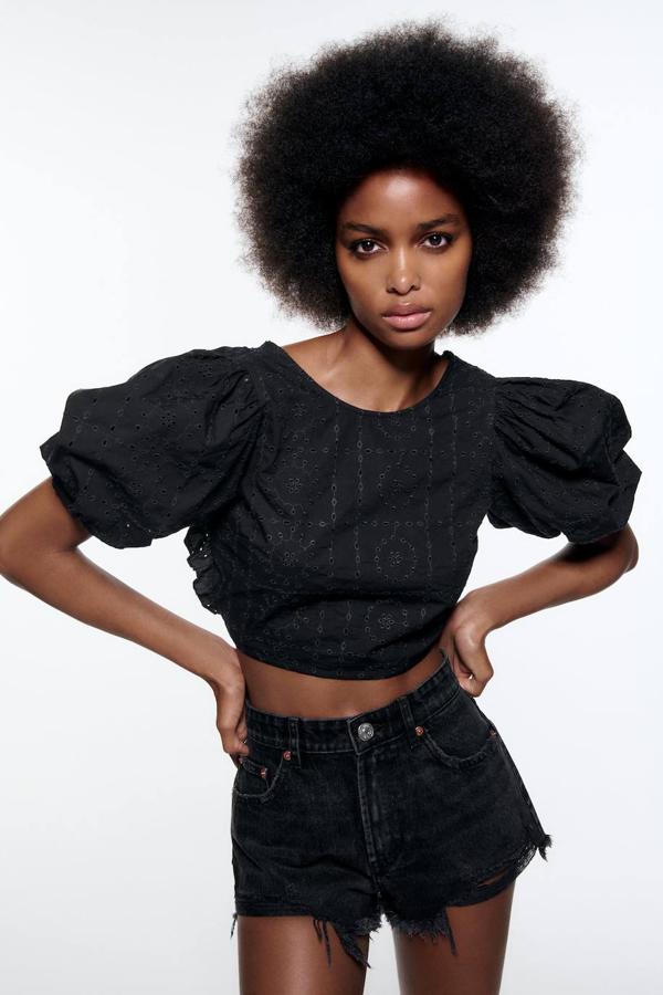Cuerpo crop en tejido bordado color negro con cuello redondo, manga corta abullonada y espalda al aire con lazada, de Zara. Puedes comprarlo en rebajas a 9,99 euros.