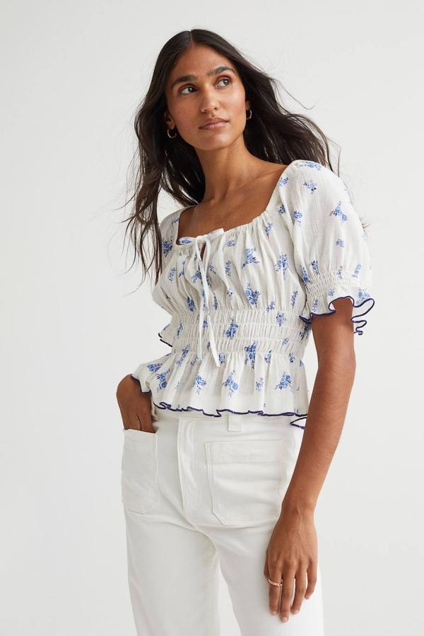 Blusa en tejido de algodón ligero con escote cuadrado, detalle de lazada, manga corta abullonada, volantes y cuerpo elástico, decorada con floral print, de H&M. Su coste es de 15,99 euros.