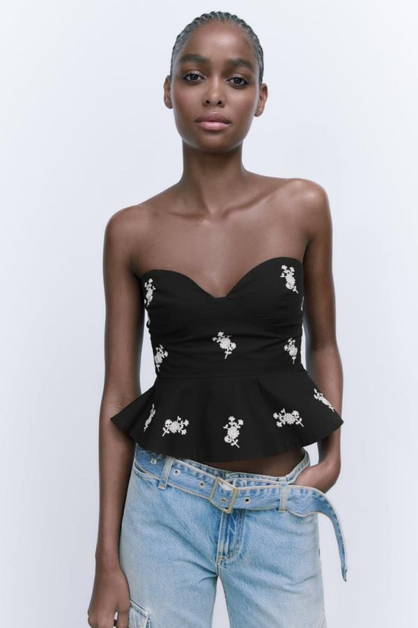 El negro es un clásico infalible que puedes actualizar añadiendo bordados de flores en color blanco. Top con escote palabra de honor de Zara (22,99 euros). 