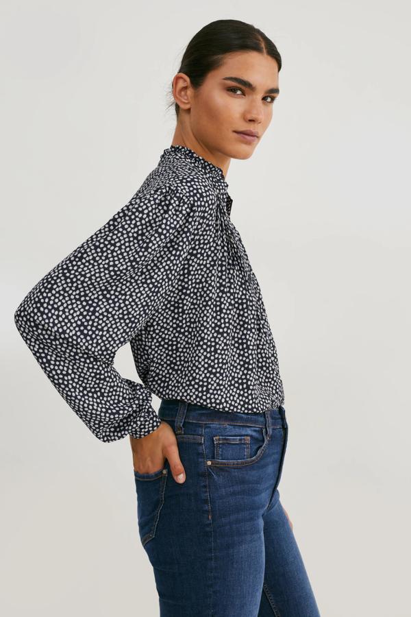 Blusa de tejido fluido con jaretas y volantes. Tiene un cuello es Mao y posee puños abotonados bombachos con un botón, además de un bajo que está redondeado. Hay que destacar el estampado original de lunares en blanco con el fondo en azul marino. Es de C&A. Precio: 19,99 €.