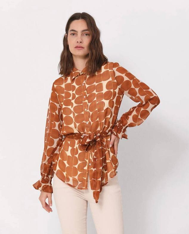 Blusón en tejido ligero y vaporoso con cuello solapa, cierre de botones, manga larga y cinturón de lazada a juego, con estampado de lunares amarillo y crudo, de Simorra. Su precio con descuento es de 79 euros.