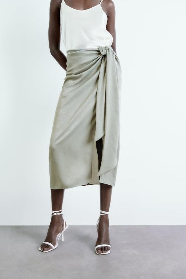 Las faldas midi más buscadas del momento son las de efecto pareo. Elige un color neutro con lazada. Falda en color gris verdoso de Zara (25,99 euros). 
