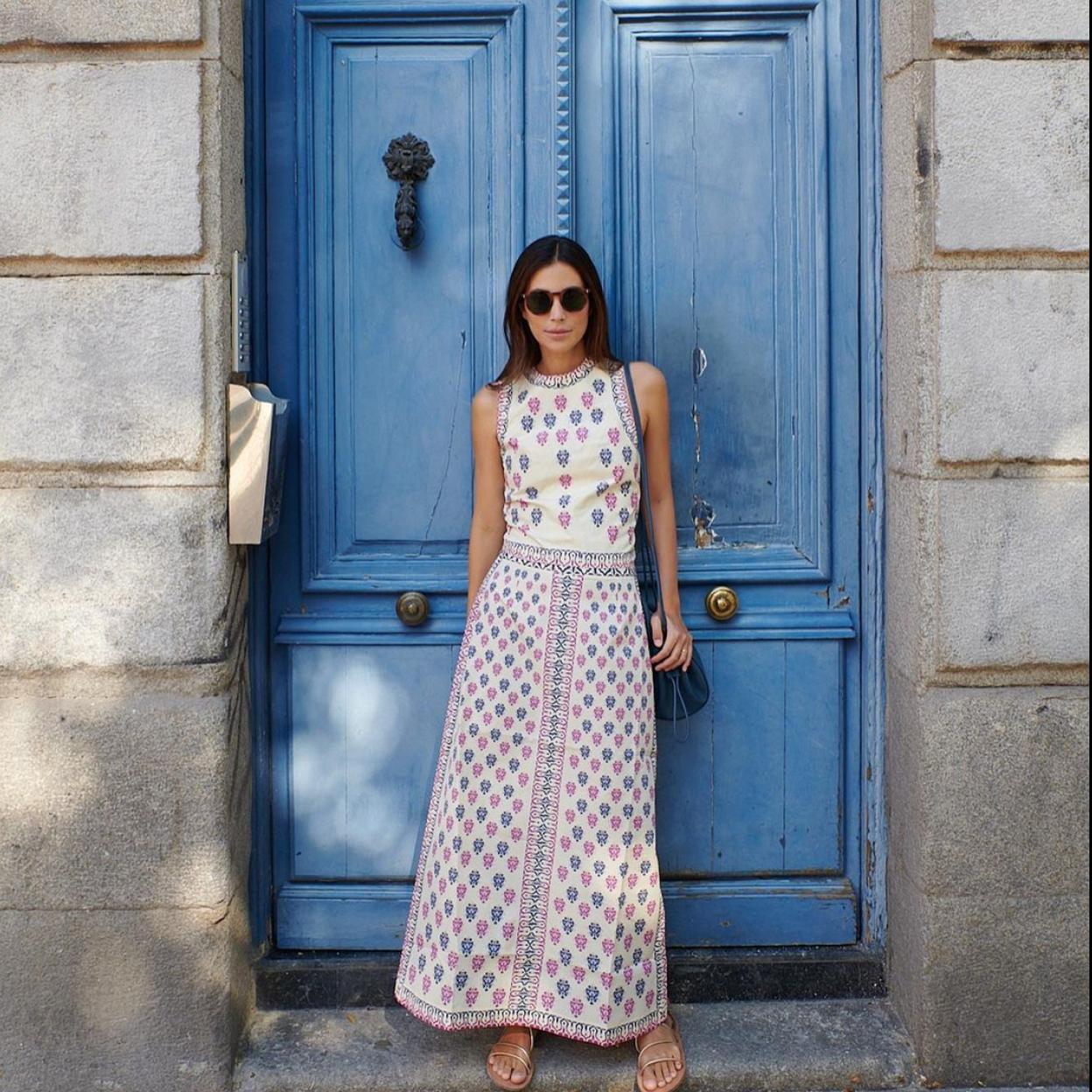 La influencer Sassa Deo posando delante de una puerta de color azul con un top y falda estampado.