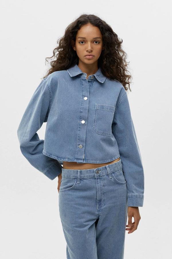 Camisa cropped vaquera con diseño ancho, cuello solapa, manga larga, bolsillo de parche y cierre de botones, con estampado a rayas azul y blanco, de Pull&Bear. Cuesta 29,99 euros.