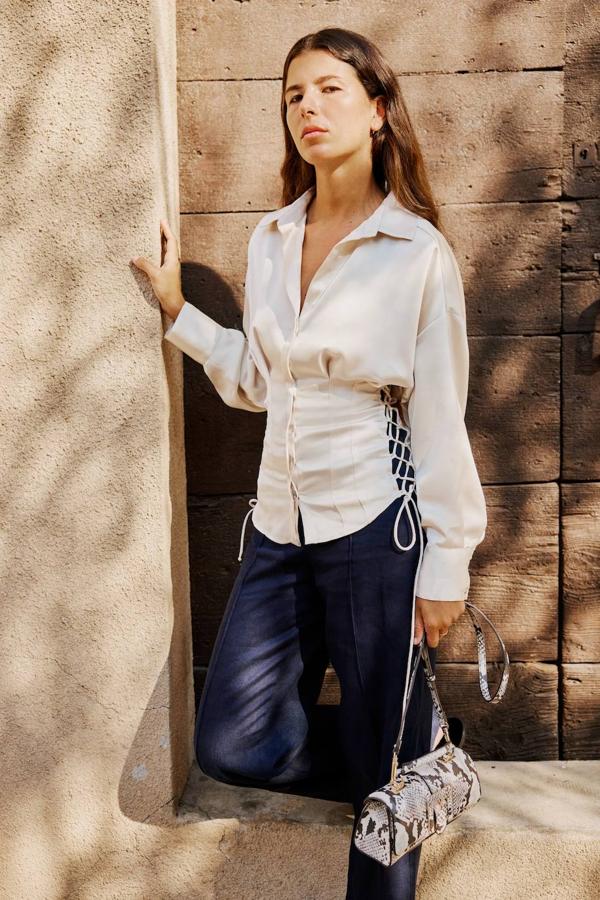 Camisa de satén estilo corsetero con cuello solapa, manga larga recogida en puño ancho, cintura entallada con detalles de pinas y cordones ajustables, silueta relajada y cierre de botones, en tono cava, de Zara. Cuesta 27,95 euros.