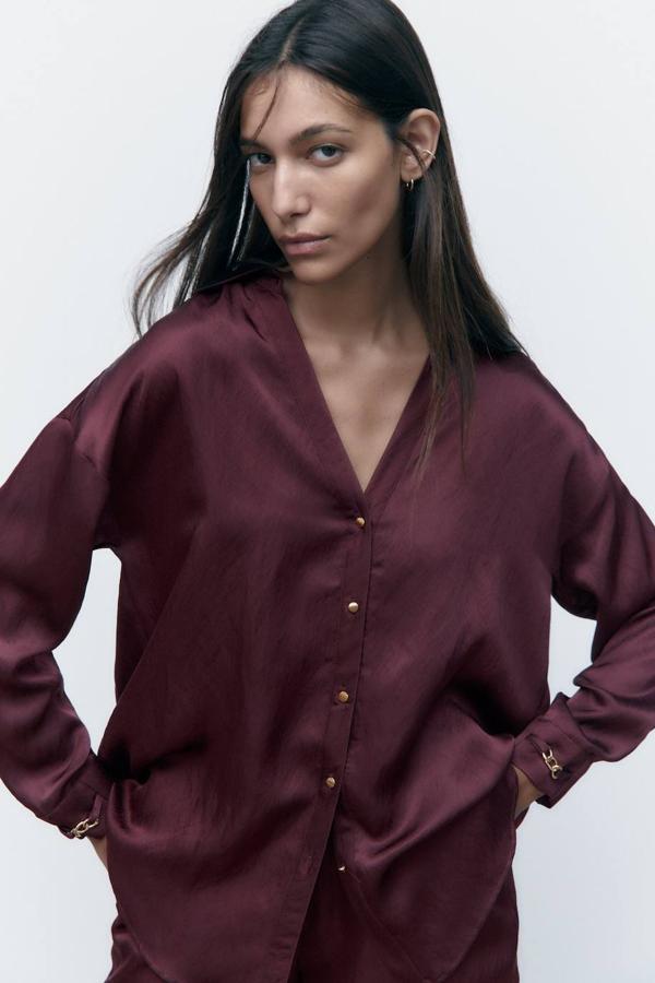 Camisa satinada con corte holgado, silueta relajada, manga larga con detalle de eslabones en los puños, cuello solapa con escote de pico y cierre de botones, tono burdeos, de Zara. La comprarás a 35,95 euros.