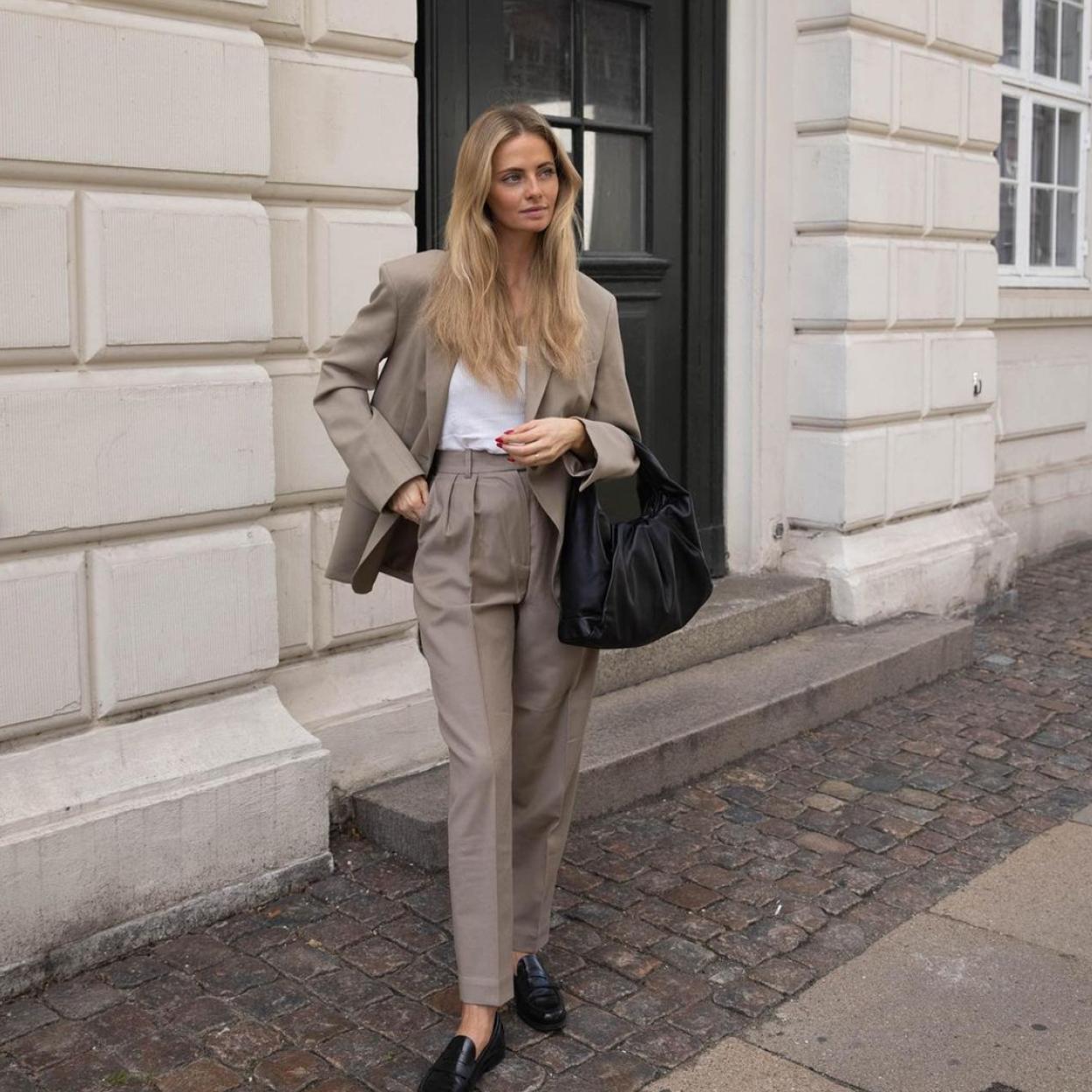 La influencer lleva un traje de color marrón que combina con una camiseta blanca y unos mocasines planos de color negro.