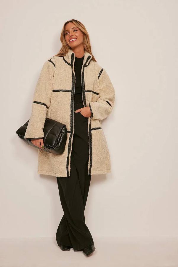Chaqueta larga de borreguillo con detalles de ribetes efecto piel a contraste, cuello elevado, manga, larga, corte oversize, cierre de cremallera y bolsillos laterales, en beige, de NA-KD. Cómprala a 74,37 euros. Cómpralo aquí