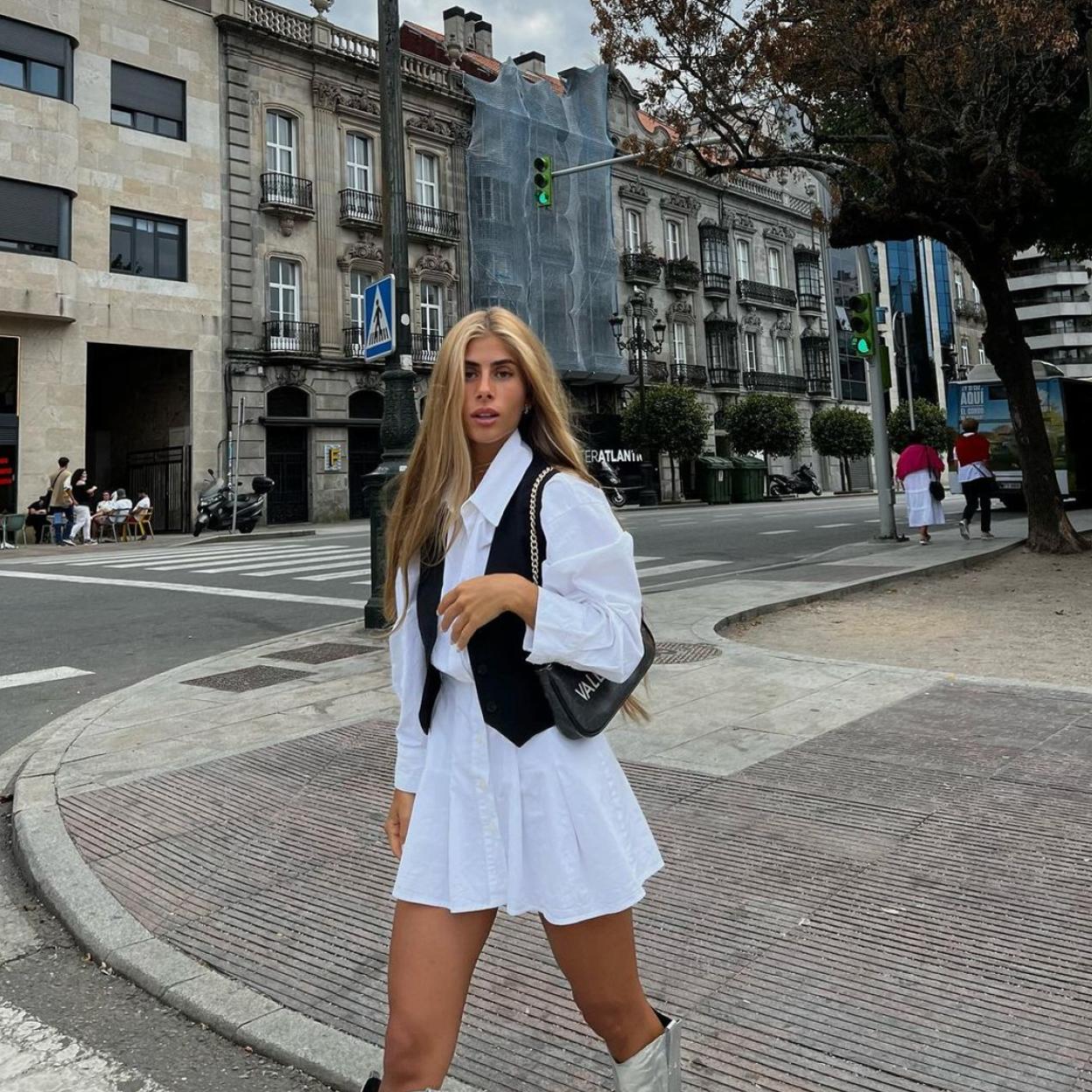 La influencer lleva un vestido blanco que combina con un chaleco negro y unas botas plateadas.