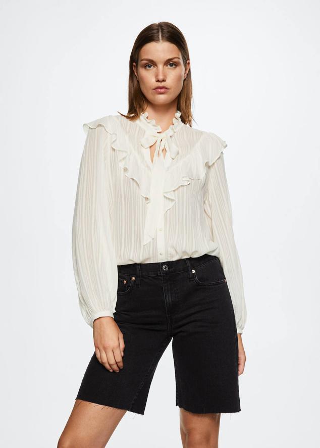 Camisa blanca en tejido ligero semitransparente con estampado de rayas a tono, manga larga ligeramente abullonada, cierre de botones, cuello subido con lazada y detalle de volantes, de Mango. Hazte con ella por 39,99 euros.