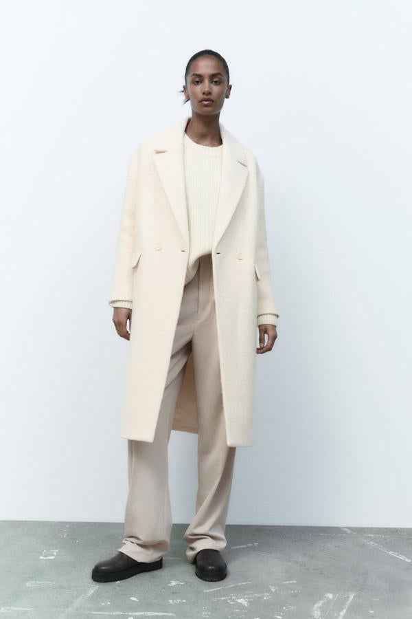 Abrigo de silueta relajada en tejido de estructura con cuello solapa, escote de pico, manga larga, cierre cruzado de botones y bolsillos con tapeta, color blanco roto, de Zara. Está disponible por 109 euros.