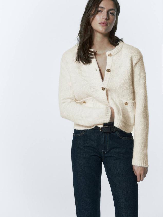 Chaqueta de punto bouclé suave con cuello redondo, manga larga, corte cuadrado, bolsillos y botones dorados, en tono crudo, de Massimo Dutti. Cuesta 99,95 euros.