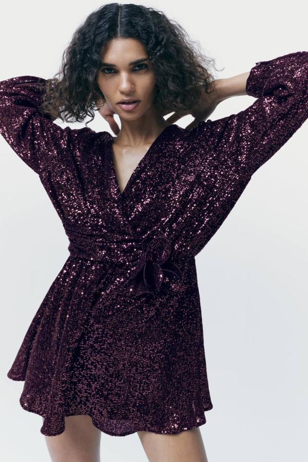 Mono corto en tejido de lentejuelas con escote de pico, manga larga, detalle de flor y bajo en evasé, color morado, de Zara. Puedes encontrarlo por 39,95 euros.