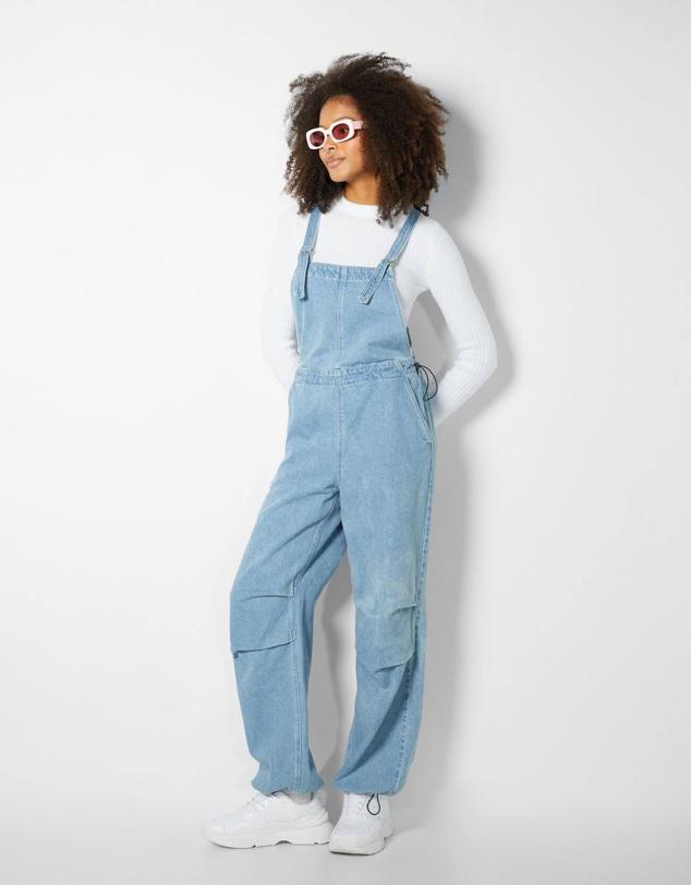 Peto denim con perneras de diseño parchute, escote cuadrado, tirantes ajustables, bolsillos y cintura elástica con stoppers, color azul, de Bershka. Hazte con él a 39,99 euros.