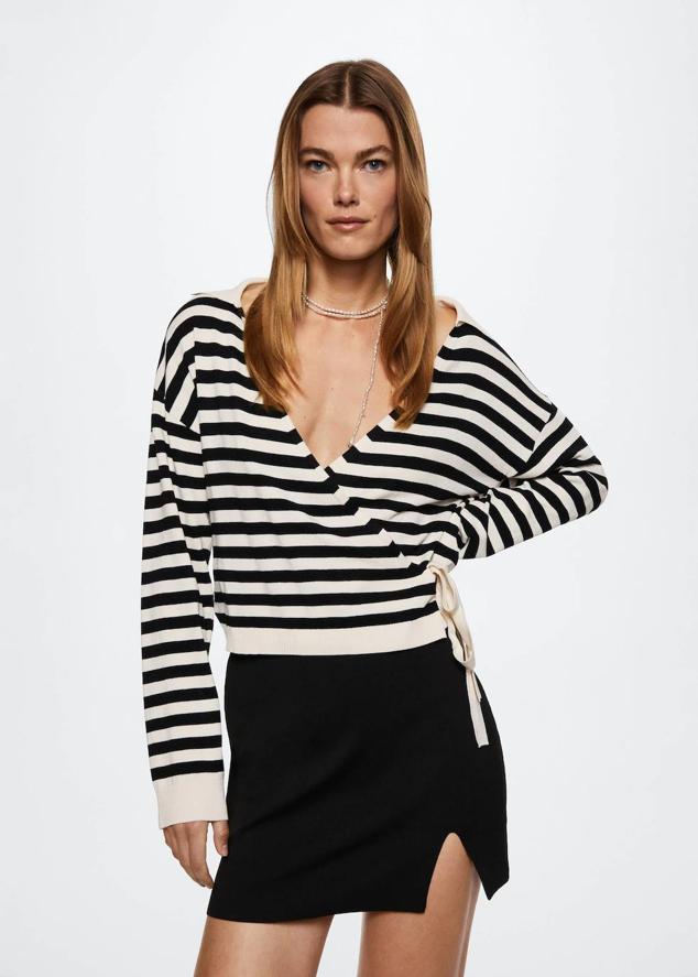 Jersey en tejido de punto fluido con cierre cruzado mediante lazada lateral, manga larga, cuello camisero y escote de pico, en print a rayas crudo y negro, de Mango. Puedes comprarlo 39,99 euros.