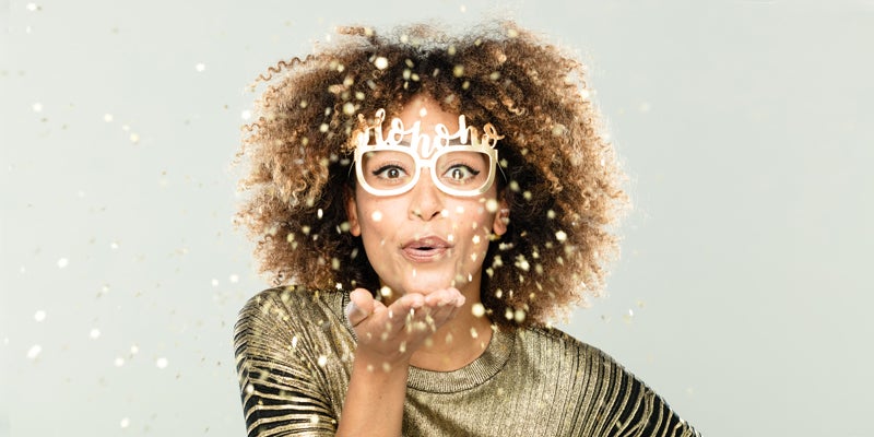 Glamour christmas portrait of happy beautiful young woman. Glamour woman wearing gold blouse and ho ho ho glasses blowing sparkles.