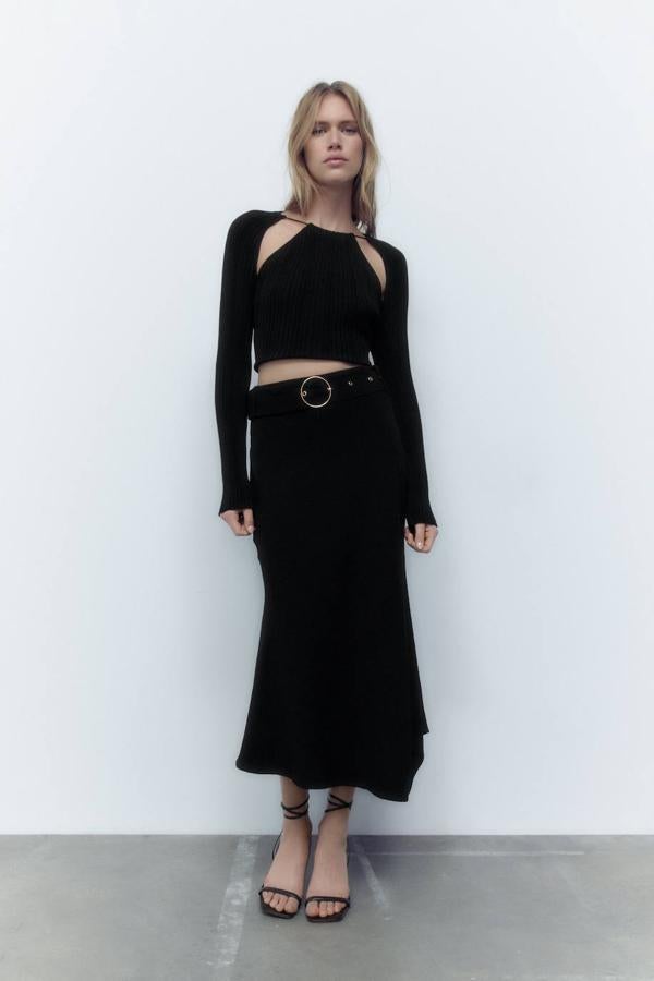 Falda midi con tiro alto, detalle de cinturón ancho y bajo asimétrico, color negro, de Zara. Hazte con ella rebajada a 19,99 euros.