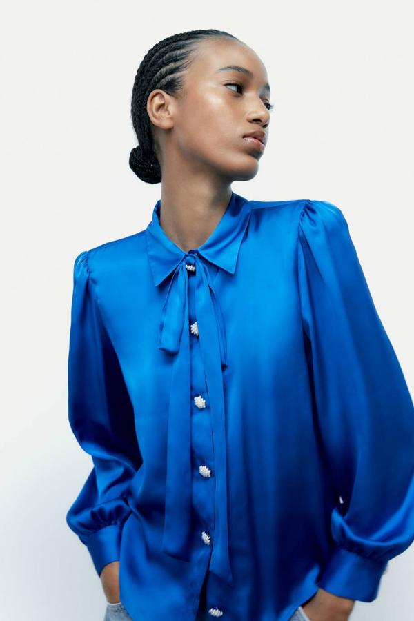 Blusa satinada con cuello solapa combinado con lazada, mangas largas abullonadas y botones joya, color azul, de Zara. Encuéntrala con descuento por 17,99 euros.