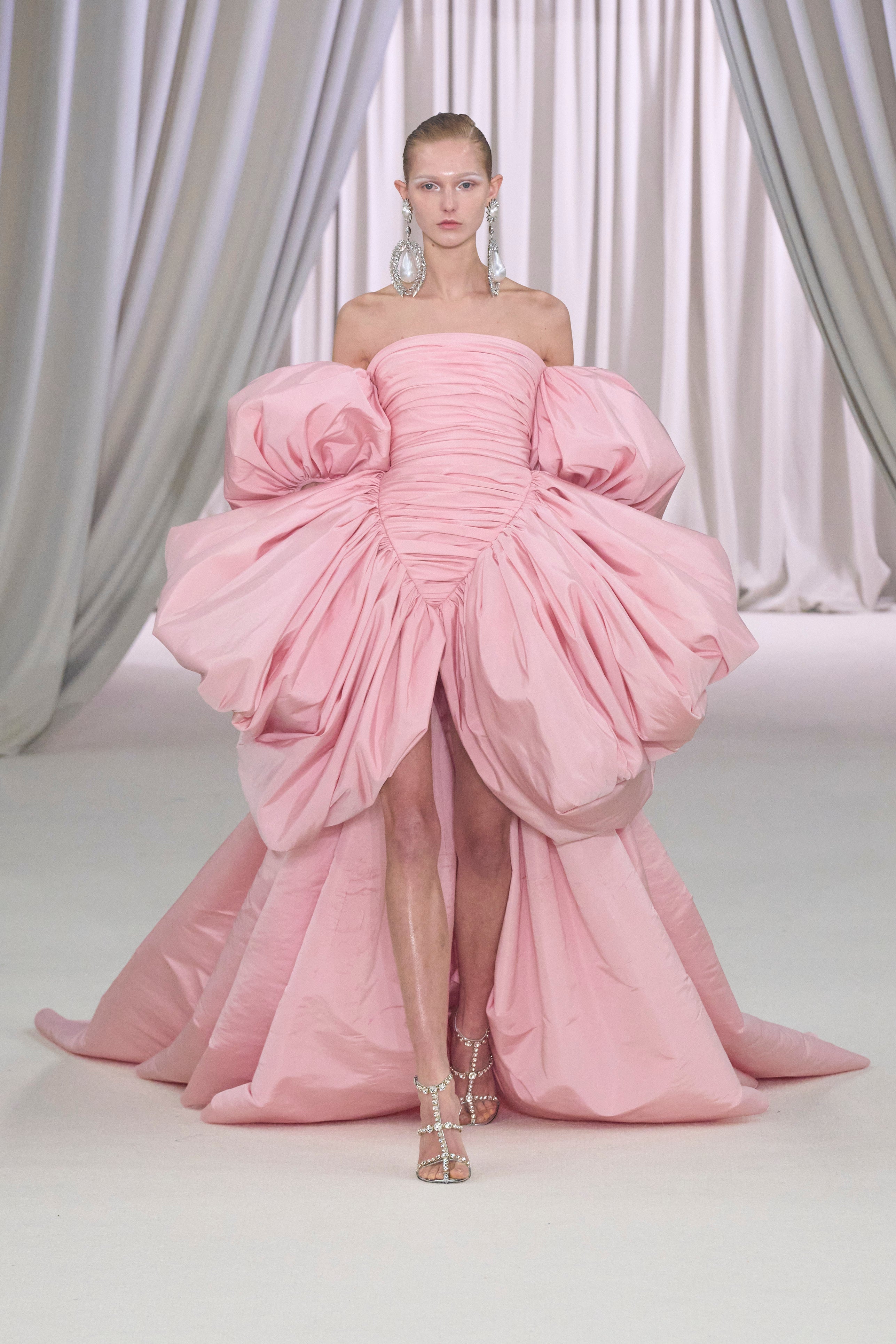 El rosa como uno de los grandes protagonistas, los volúmenes y drapeados que beben directamente de la estética ochentera, los escotes off the shoulders, los largos asimétricos... Este vestido es ADN Valli puro. 