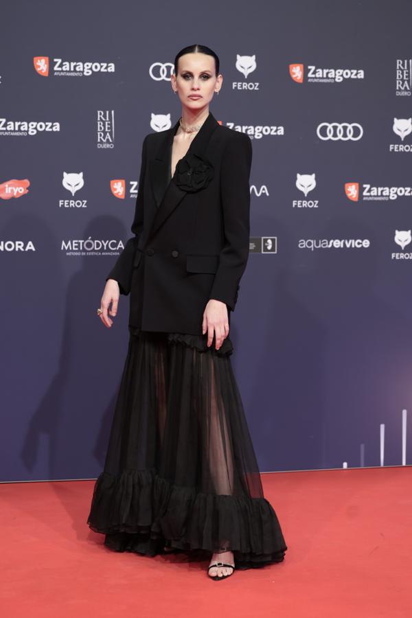 Milena Smit no nos ha defraudado con su look más sexi y total black. Ha combinado un vestido de tul con transparencias en la falda y con un blazer. Además, luce joyas discretas para ponerle broche de oro a un look soberbio. 