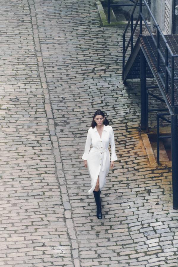 Vestido camisero midi con manga larga terminada en puño, cuello solapa, detalles de trabillas, botones dorados y cinturón ajustable, en crudo, de Zara. Su precio es de 45,95 euros.