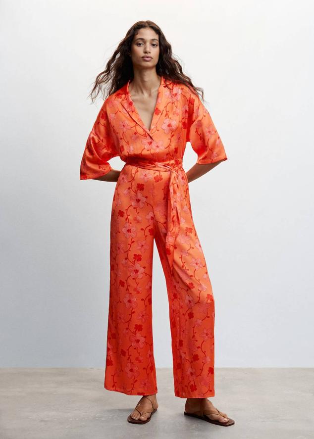 Mono en tejido fluido satinado con perneras anchas, manga corta, cuello solapa y cinturón de lazada a juego, en floral print naranja. Puedes encontrarlo a 59,99 euros.
