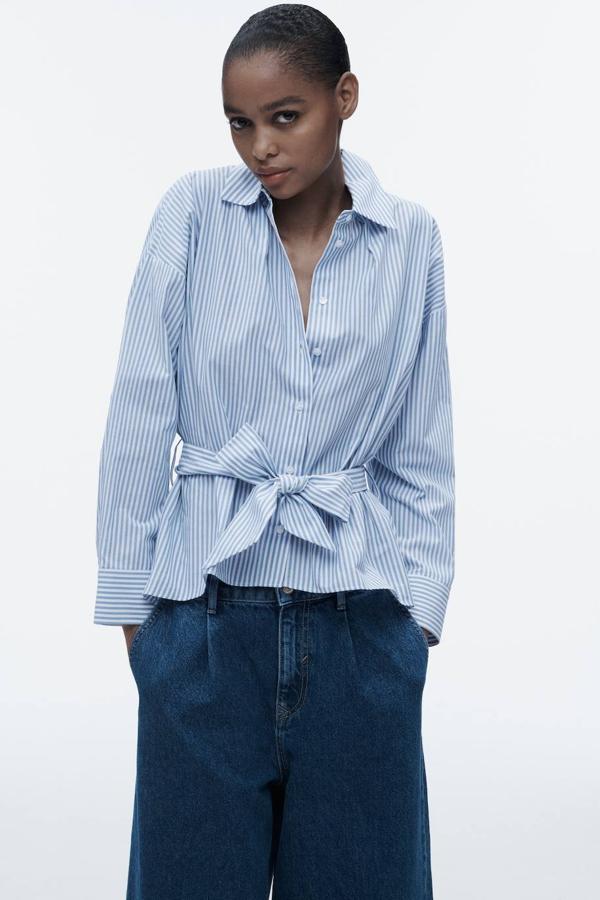 Camisa con cuello solapa, manga larga, cierre frontal de botones y detalle de cinturón de lazada a juego, en blanco y azul claro, de Zara. Su precio es de 27,95 euros.