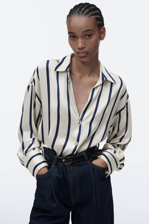 Camisa en tejido satinado fluido con cuello solapa, manga larga y cierre de botones, en estampado de rayas finas crudo y marino, de Zara. Puedes encontrarla a 25,95 euros.