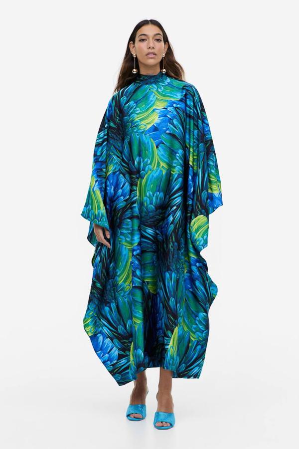 Vestido largo en tejido de satén con cuello elevado, mangas anchas y estampado de plumas en azul y verde. Cuesta 44,99 euros.