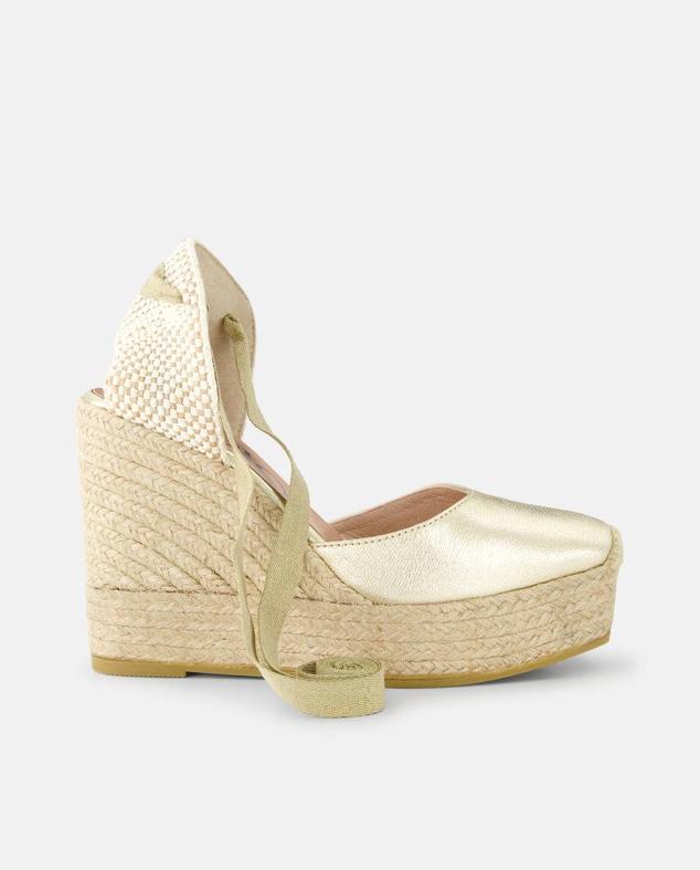 Alpargatas con cuña de yute, tejido efecto metalizado, punta redondo y lazada al tobillo, en dorado, de Gaimo. Puedes comprarlas en El Corte Inglés por 89 euros.