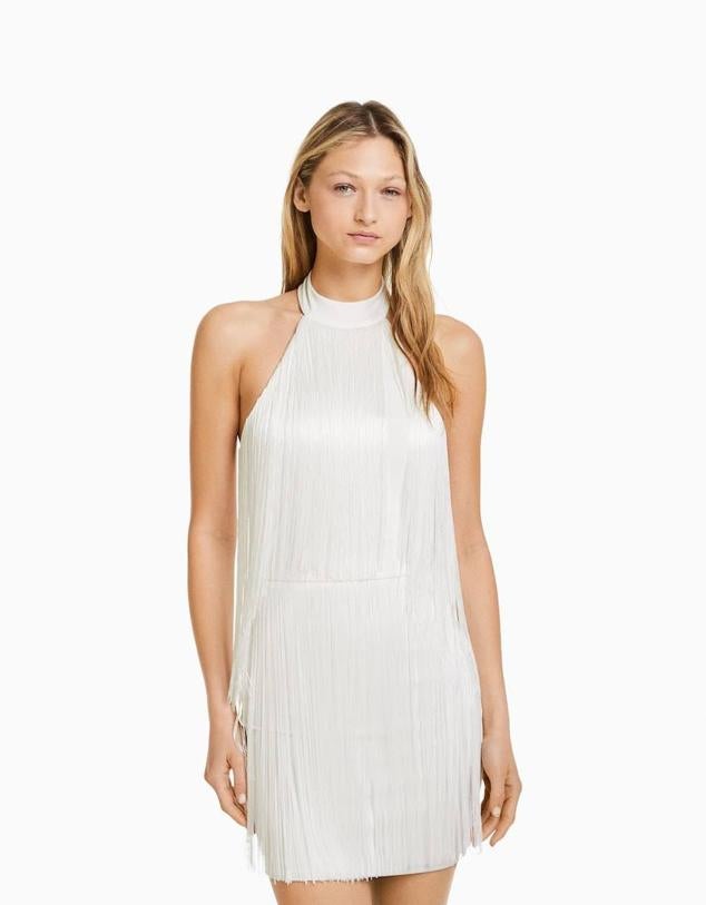 Vestido corto en tejido decorado con flecos y cuello halter, color blanco, de Bershka. Puedes encontrarlo a 29,99 euros.