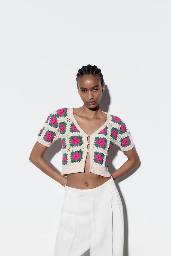 Top en tejido de punto crochet con corte cropped, manga corta, cierre de botones y escote de pico, en patrón con flores crudo, rosa y verde, de Zara. Cómpralo a 35,95 euros.