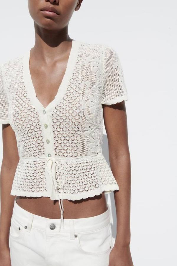 Top de crochet con escote de pico, manga corta, cierre de botones, detalle de cordón y bajo en volante destoneado, color blanco, de Zara. Puedes encontrarlo por 22,95 euros.