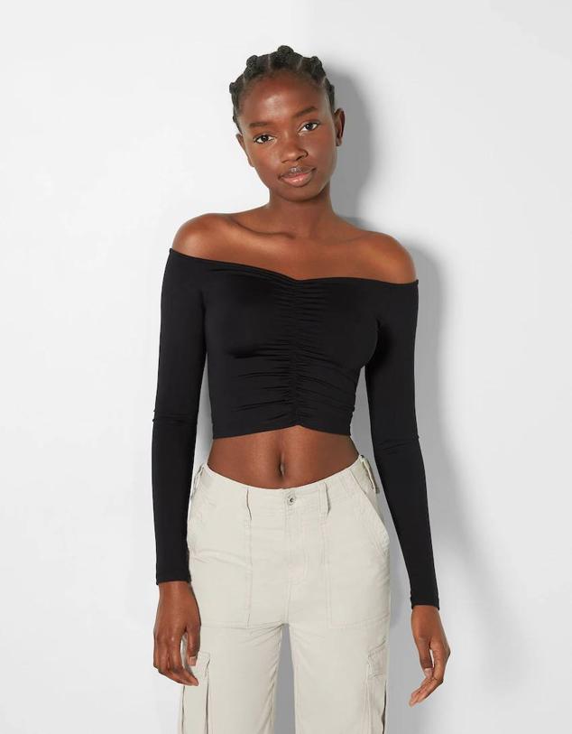Camiseta elástica entallada con manga larga, escote bardot con hombros al descubierto y detalle fruncido, tono negro, de Bershka. Hazte con ella por 12,99 euros.