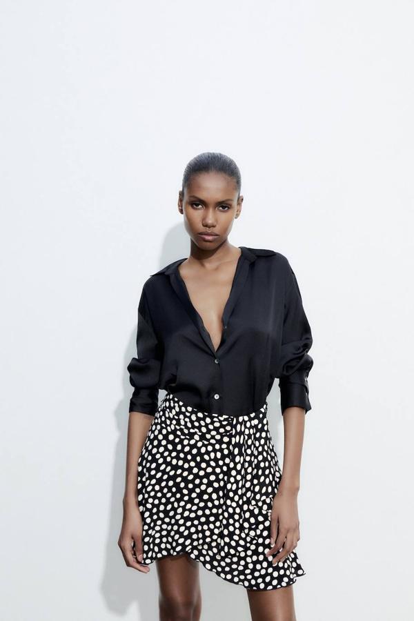 Falda corta con diseño cruzado, pliegues en la cintura, tiro alto y bajo acabado en volantes, con print de lunares blanco y negro. Puedes encontrarla por 25,95 euros.