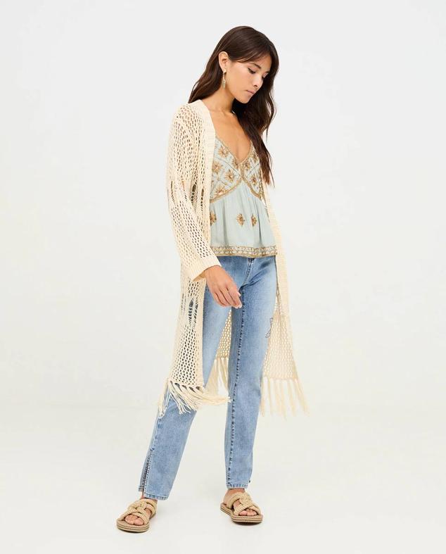 Chaqueta larga en tejido de punto calado con diseño abierto, manga larga y bajo terminado en flecos, tono crudo, de NKN Nekane. Está disponible en El Corte Inglés a 75 euros.