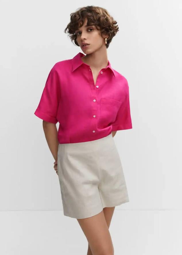 Camisa de lino oversize con cuello solapa, manga corta, bolsillos plastrón y cierre de botones, tono fucsia, de Mango. Cuesta 27,99 euros.