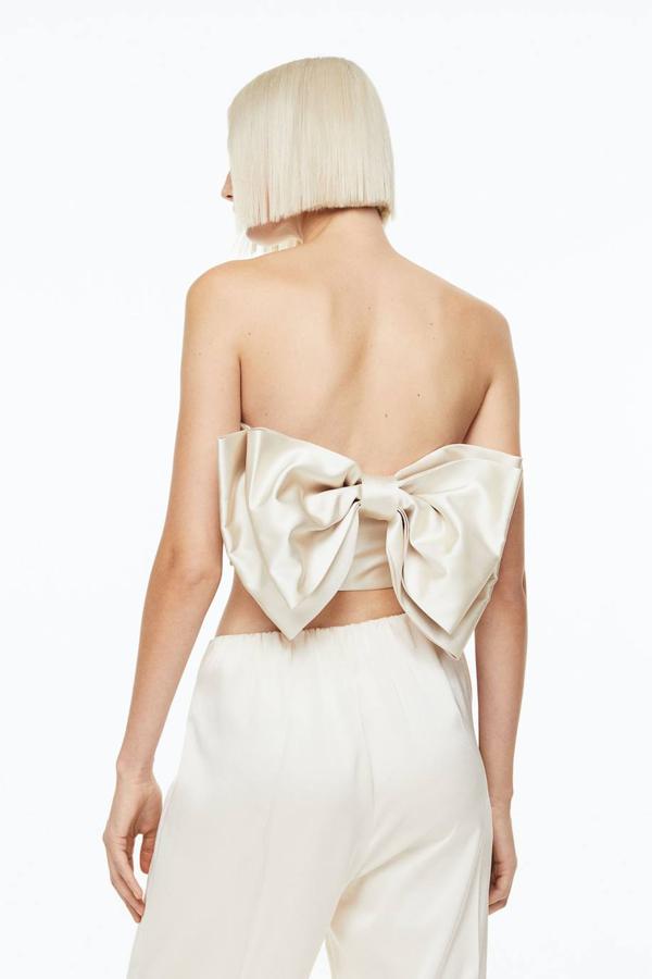 Top cropped satinado con escote recto, tirantes finos y maxi lazo en la espalda, color beige, de H&M. Está disponible por 26,99 euros.